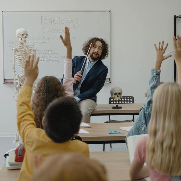 Teacher sitting on the desk in the classroom and teaching kids.